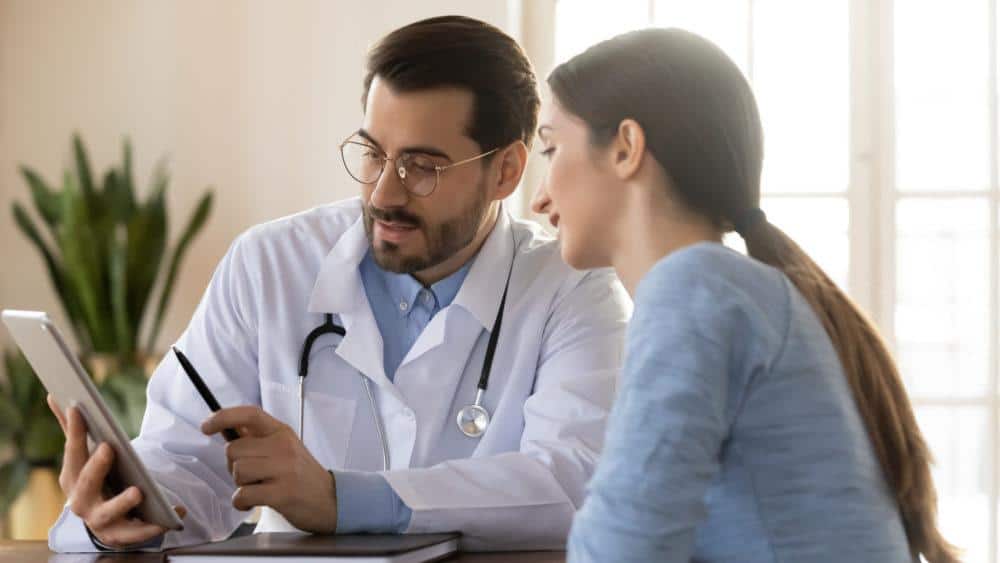A Doctor is Talking to a Patient While Looking at a Tablet