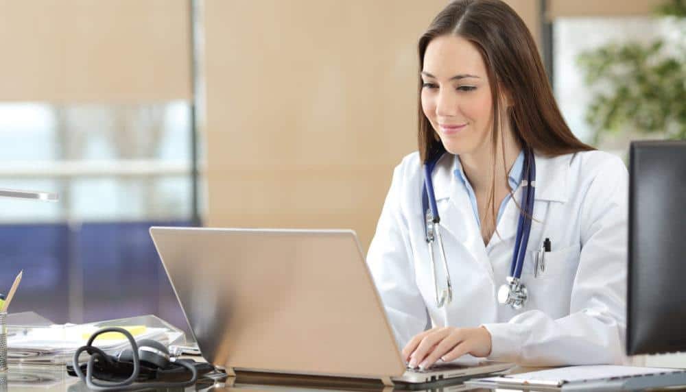 a doctor is sitting at a desk using a laptop computer
