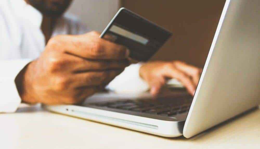 a man is typing on a laptop while holding a credit card