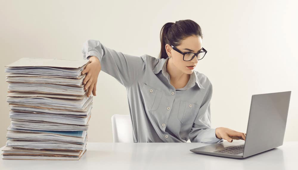 a woman sitting at a desk with a stack of papers and a laptop