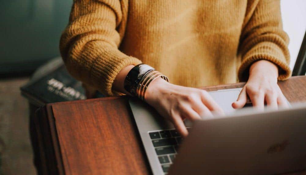 a woman in a yellow sweater is typing on a laptop