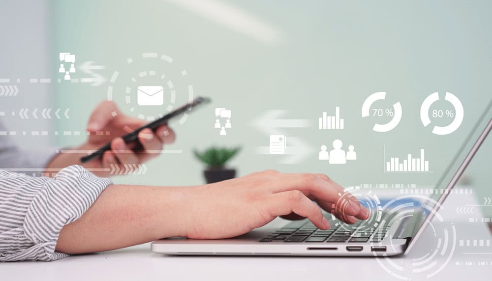 a person is typing on a laptop while holding a cell phone