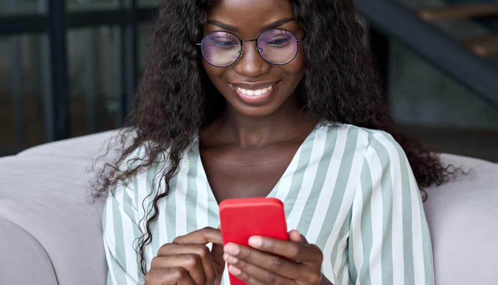 a woman wearing glasses is sitting on a couch using a cell phone