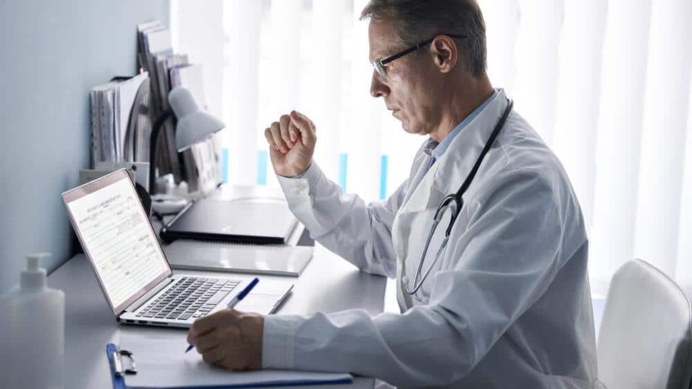 a doctor is sitting at a desk in front of a laptop computer